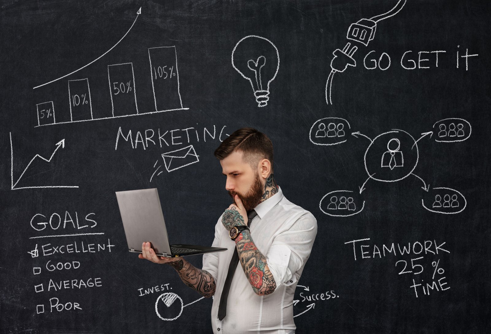 Tattooed bearded techer with laptop over school desk with formulas.